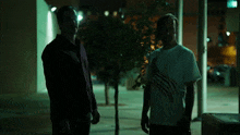 two men standing next to each other with one wearing a white shirt with a claw print