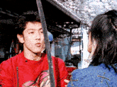 a man in a red shirt is holding a sword and talking to a woman in a blue jacket