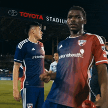 two soccer players standing in front of a toyota stadium banner