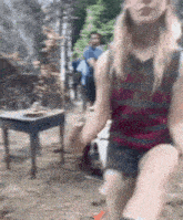 a woman in a striped tank top and shorts is standing in the dirt