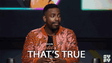 a man in a floral jacket is sitting in front of a sign that says that 's true