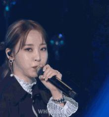 a woman is singing into a microphone while wearing a jacket and earrings .