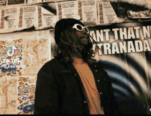 a man wearing sunglasses and a hat stands in front of a poster that says ant that n't granada