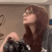a woman wearing glasses is holding a camera .