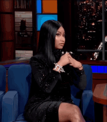 a woman in a black dress is sitting in a chair with her legs crossed and clapping her hands .