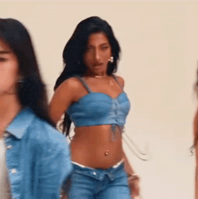 a woman in a blue crop top and jeans is standing next to a woman in a blue jacket .