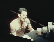 a shirtless man singing into a microphone while sitting at a table
