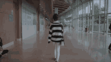 a woman in a black and white striped sweater is walking down a hallway with people sitting on the floor .