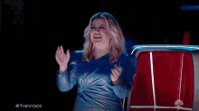 a woman in a blue dress is standing in front of a red curtain and applauding .