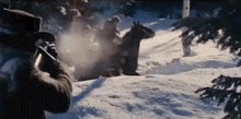 a man in a top hat is holding a gun in the snow while a man on a horse is riding by .