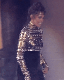 a woman in a black and gold outfit is walking on a stage