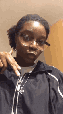 a woman wearing glasses and a black jacket has a heart necklace