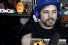 a man wearing headphones and a blue hat is sitting in front of a microphone in a room .