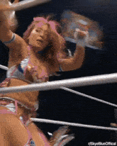 a woman with pink hair is standing in a wrestling ring holding a trophy .