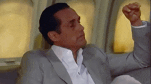 a man in a suit is sitting on a couch with his fist in the air