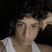 a young man with curly hair wearing headphones and a white tank top