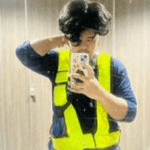 a man in a yellow vest is taking a selfie with his cell phone .