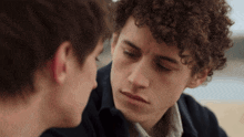a man with curly hair looks at another man