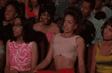 a woman in a crop top is sitting in a crowd of people watching a show .
