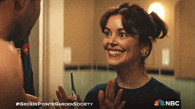 a woman is smiling while looking at herself in a mirror with a nbc logo in the corner
