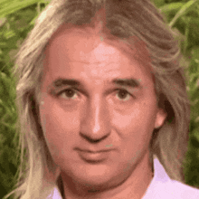 a close up of a man 's face with long blonde hair and a white shirt .