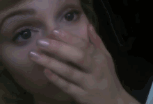 a woman covering her mouth with her hand while looking at the camera