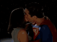 a man in a superman costume is kissing a woman in a white tank top .