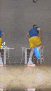 a man in a blue shirt and yellow shorts is dancing in front of a table and chairs .