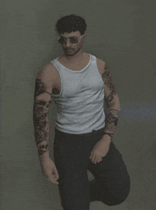 a man in a white tank top and black pants has a tattoo on his arm