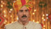 a man with a mustache is wearing a colorful turban and looking at the camera .
