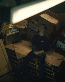 a man sits on a pallet surrounded by boxes including a dada box