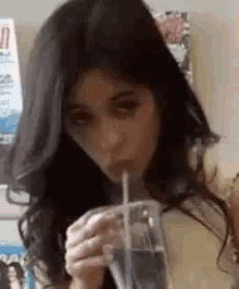 a woman is drinking from a glass with a straw .