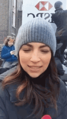 a woman wearing a beanie stands in front of a white truck that says hsbc