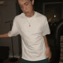 a young man wearing a white t-shirt and a necklace with a letter b on it