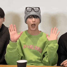 a young man wearing a green sweatshirt and a supreme hat