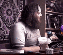 a man with long hair and a beard is sitting at a table holding a piece of paper