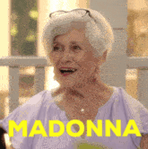 an elderly woman wearing glasses and a purple shirt with the word madonna in yellow
