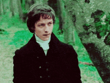 a man in a black jacket and white shirt is standing in the woods .