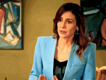 a woman in a blue jacket stands in front of a painting on the wall