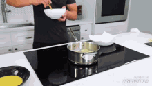 a man is cooking on an induction stove with a bowl of food in his hand .