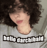 a woman with curly hair is wearing a gray shirt that says hello darchibald .