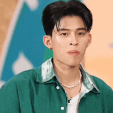 a young man wearing a green shirt and a pearl necklace looks at the camera .