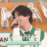 a man in a green vest and tie is singing into a microphone and smiling .