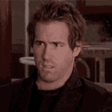 a man in a black jacket is making a funny face while looking at the camera .