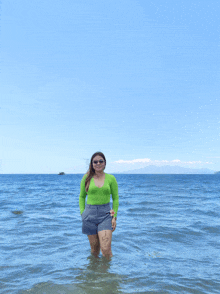 a woman in a green top and gray shorts stands in the ocean