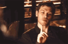 a man in a suit and tie is sitting in a dark room with his hand on his chin