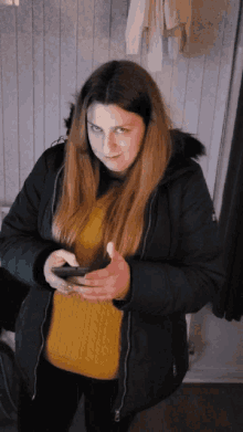a woman wearing a black coat and a yellow sweater is looking at her phone