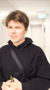 a man in a black hoodie is standing in a hallway with the exit sign above him
