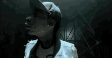 a man wearing a hat and a denim vest is standing in the dark .