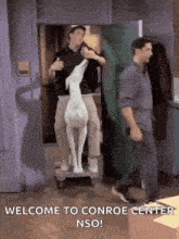 two men are pushing a statue of a deer on a cart with the words welcome to conroe center nso written below them